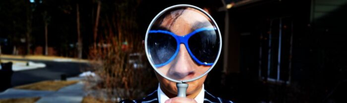 person looking to the camera through magnyfying glass